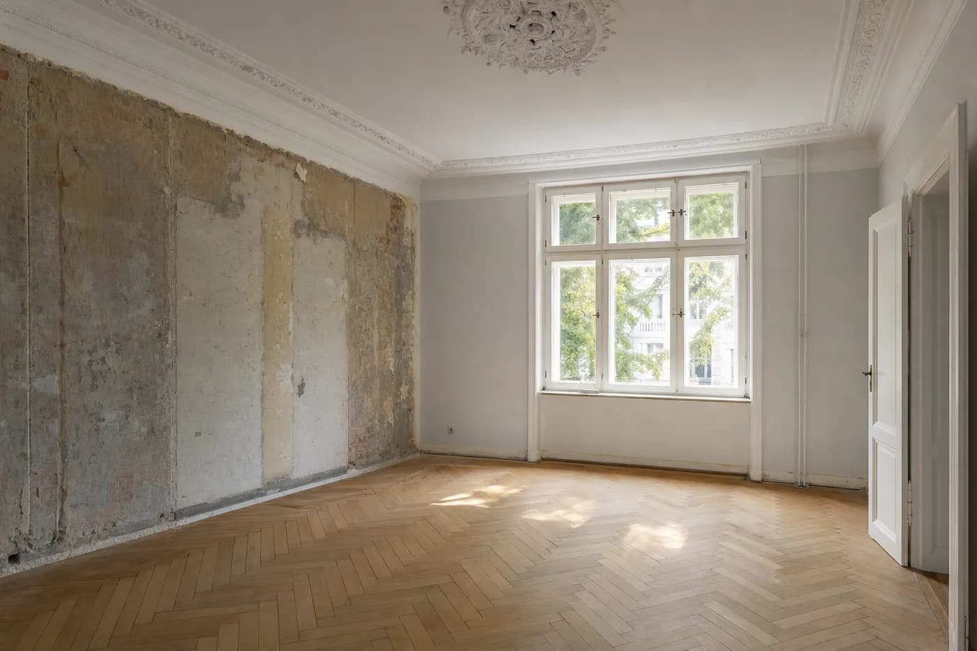Altbauzimmer während der Sanierung: Stuckdecke mit Rosette, aufgearbeitetes Fischgrätparkett und eine bis auf den alten Putz freigelegte Wand