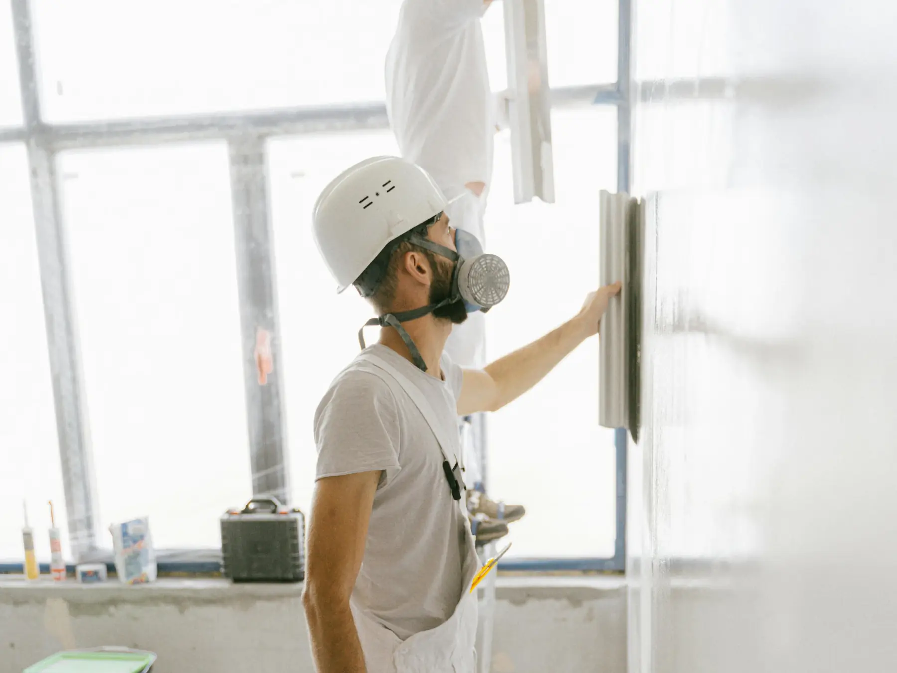 Zwei Handwerker in weißer Arbeitskleidung ziehen eine Wand glatt – Konzentriert auf das Gewerk, nicht auf den Papierkram